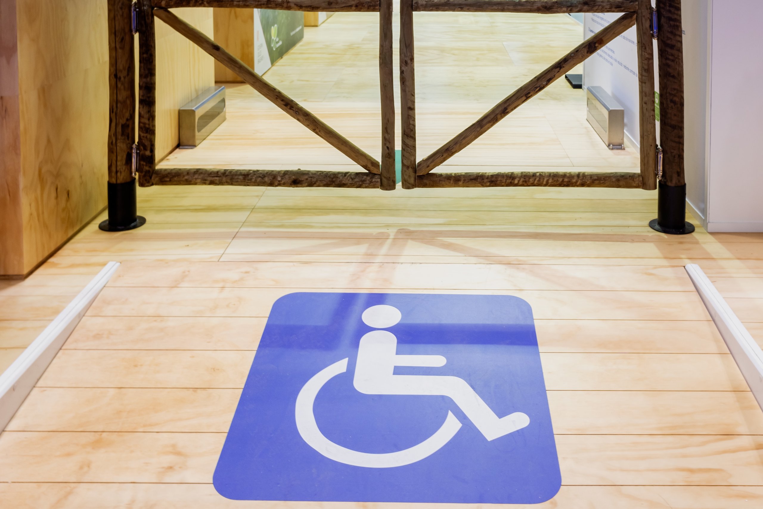 Blue and white wheelchair accessibility symbol painted on a light wooden floor in front of a wooden gate.