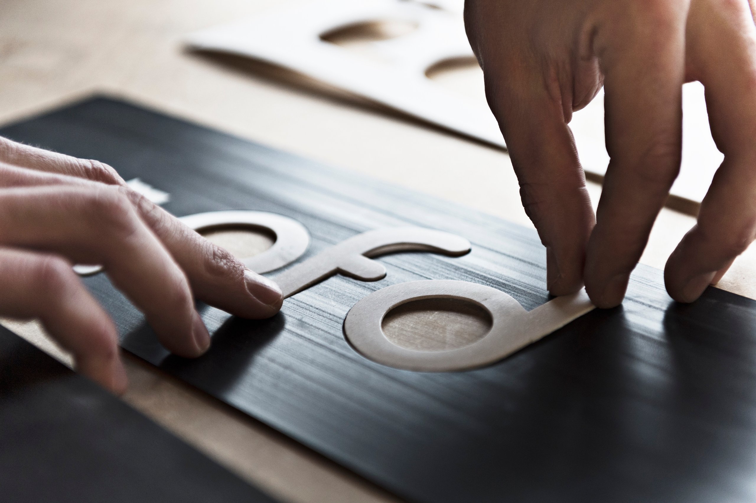 Two hands arranging cardboard letters on a black surface.