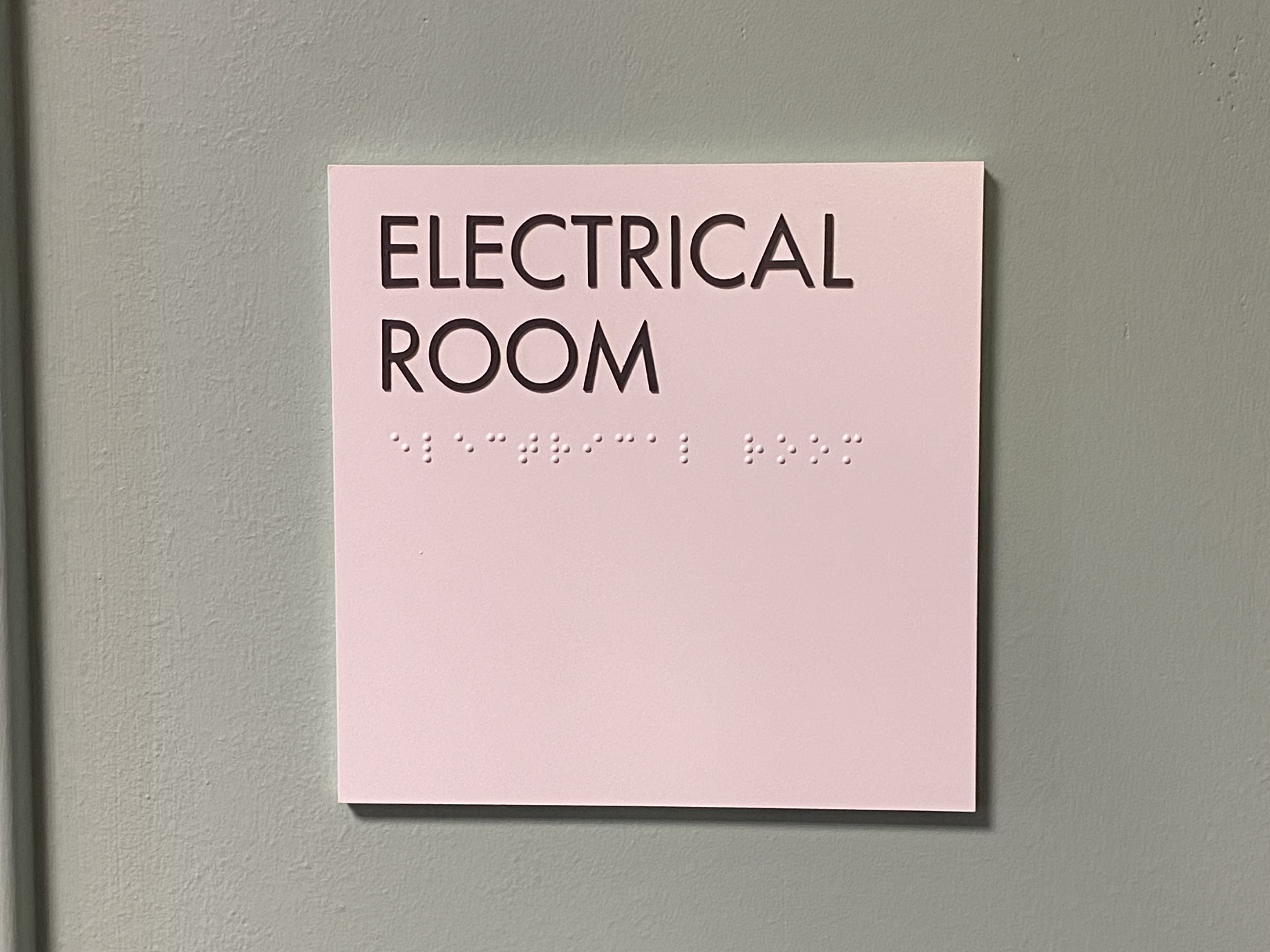 Sign on gray wall reading 'ELECTRICAL ROOM' with Braille text below.