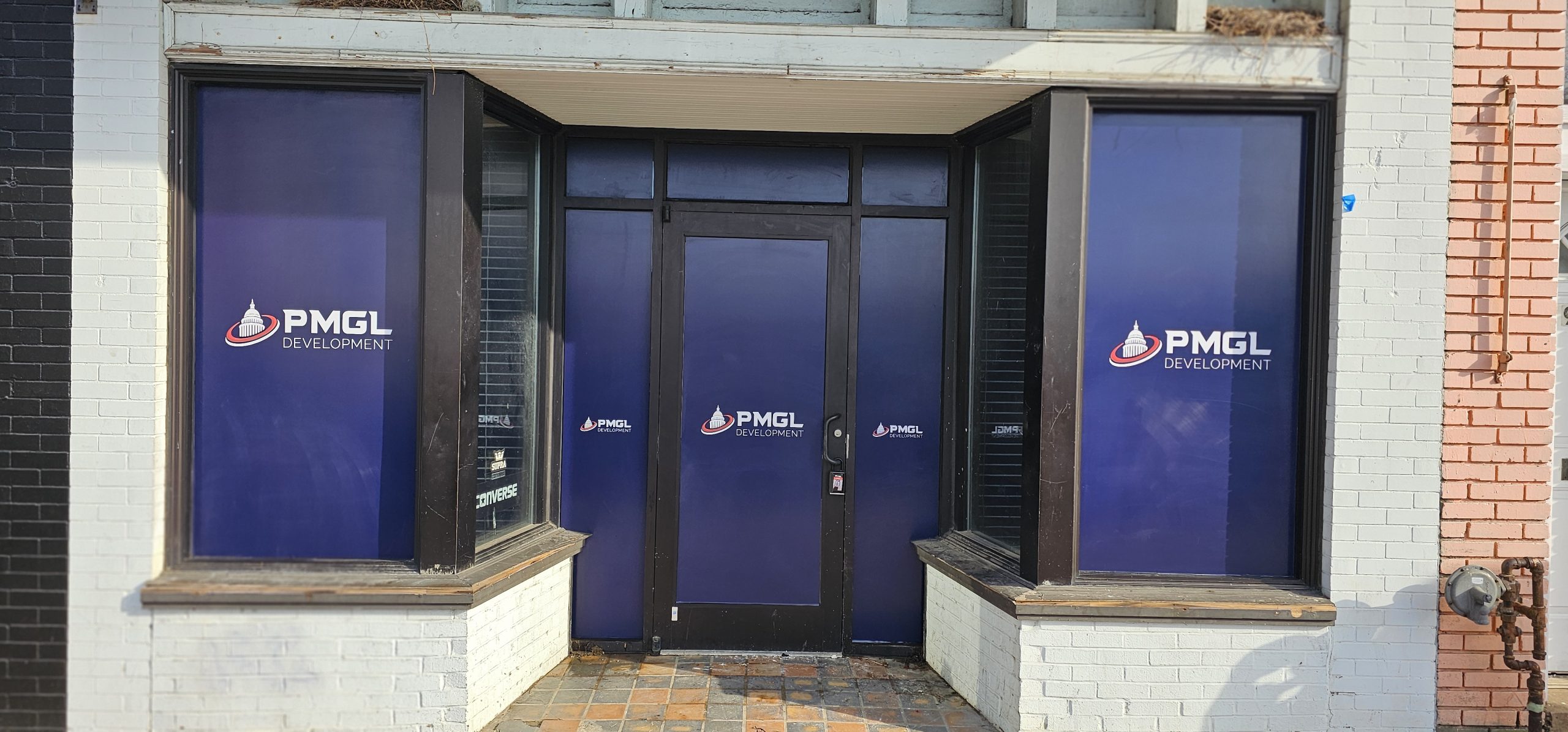 Storefront with black-framed glass door and windows covered in blue panels featuring the PMGL Development logo.