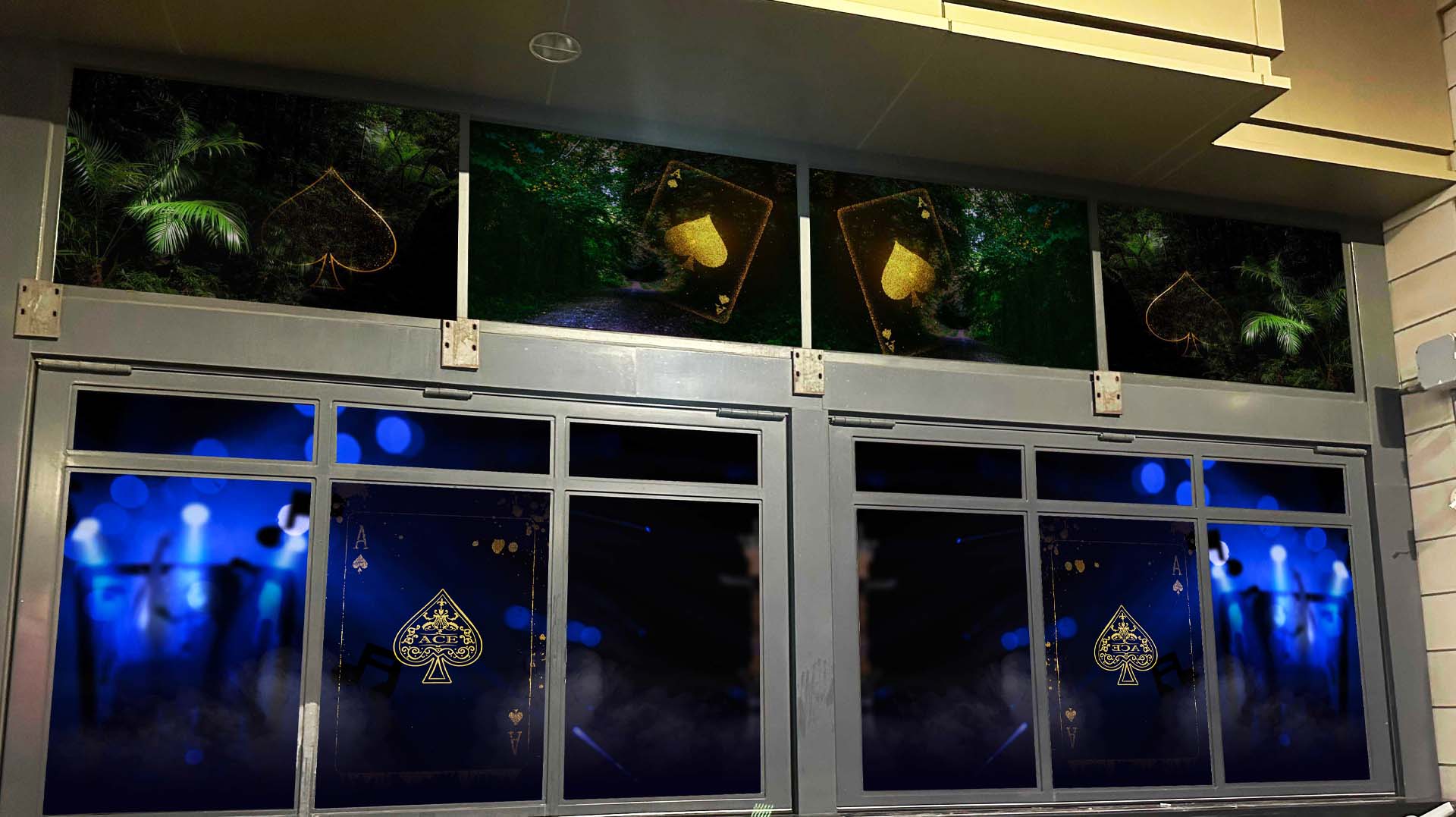 Two large Ace of Spades cards displayed on glass windows with dark blue bokeh lights and smoke effects, and smaller spade symbols above framed by greenery.
