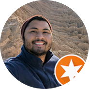 Smiling man with a beard wearing a dark jacket and beanie, standing in a rocky outdoor setting with a Google Local Guide badge.