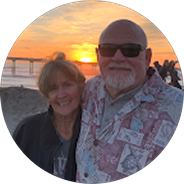 An older couple smiling at the camera at the beach during sunset.
