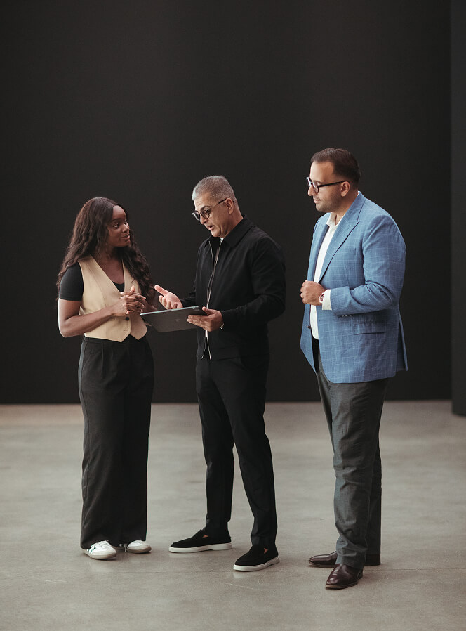 Three professionals standing and discussing, one holding a tablet.