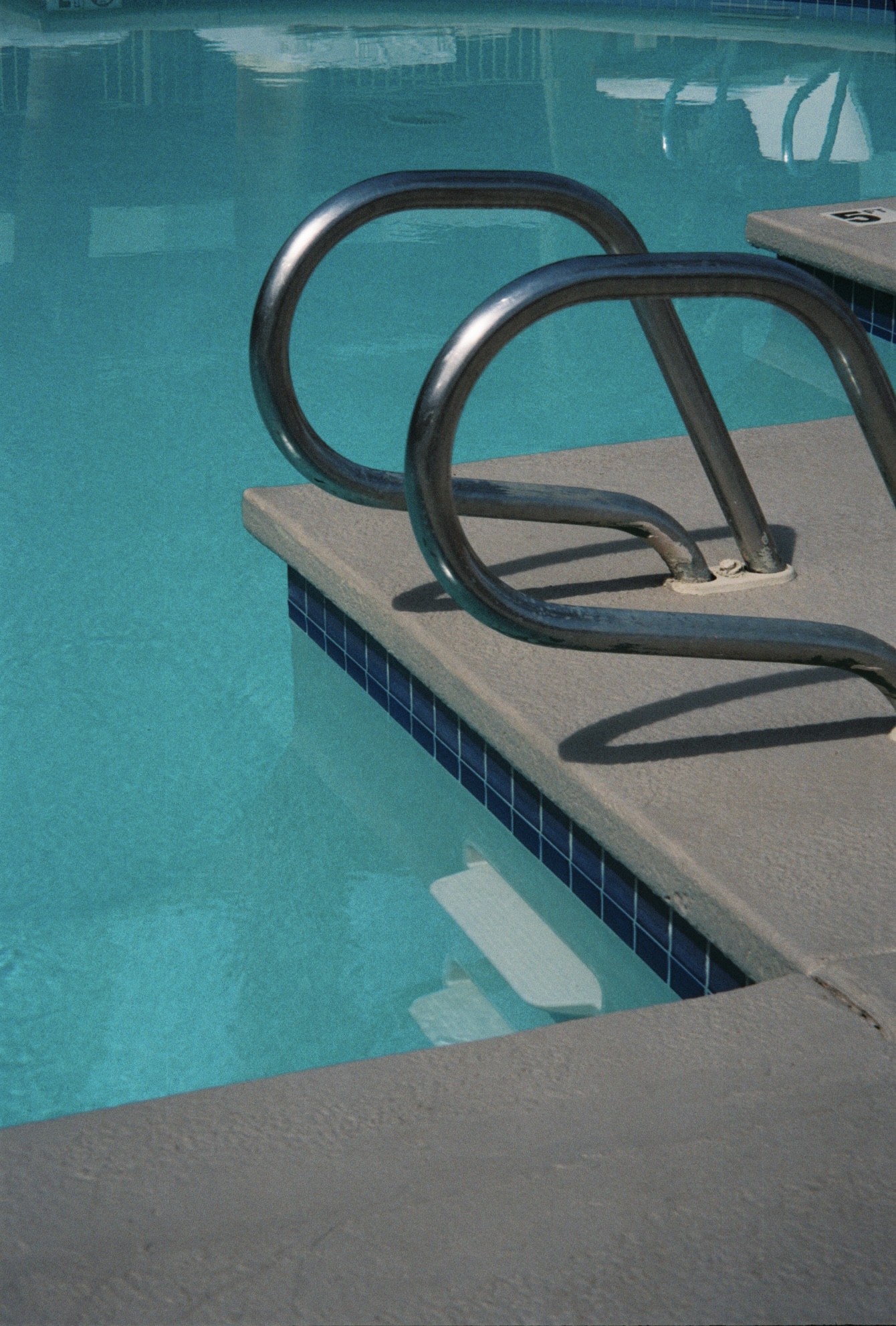 Close-up of metal handrails and steps descending into a clear blue swimming pool.