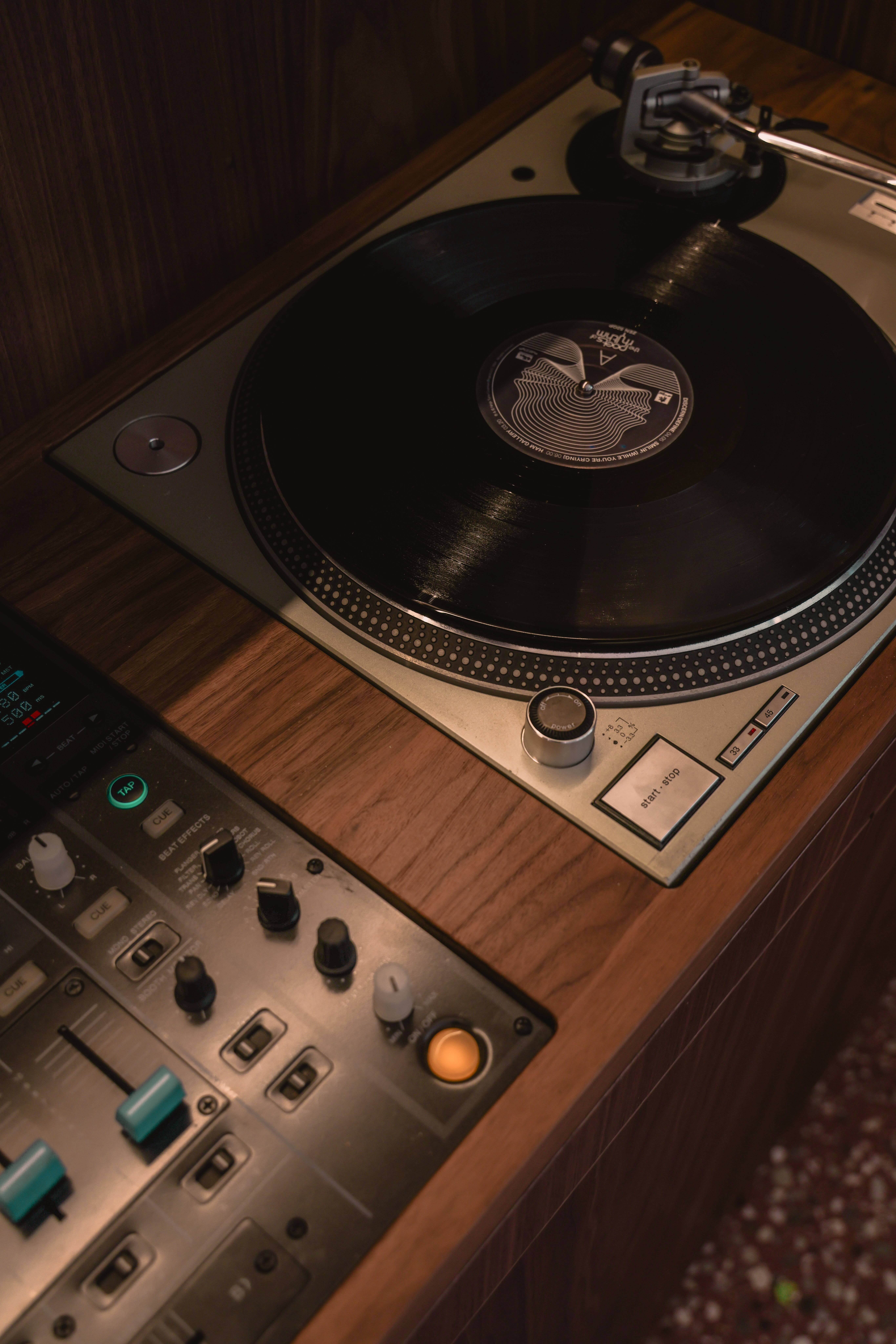 Close-up of a vintage turntable playing a vinyl record next to a DJ mixer with sliders and knobs.