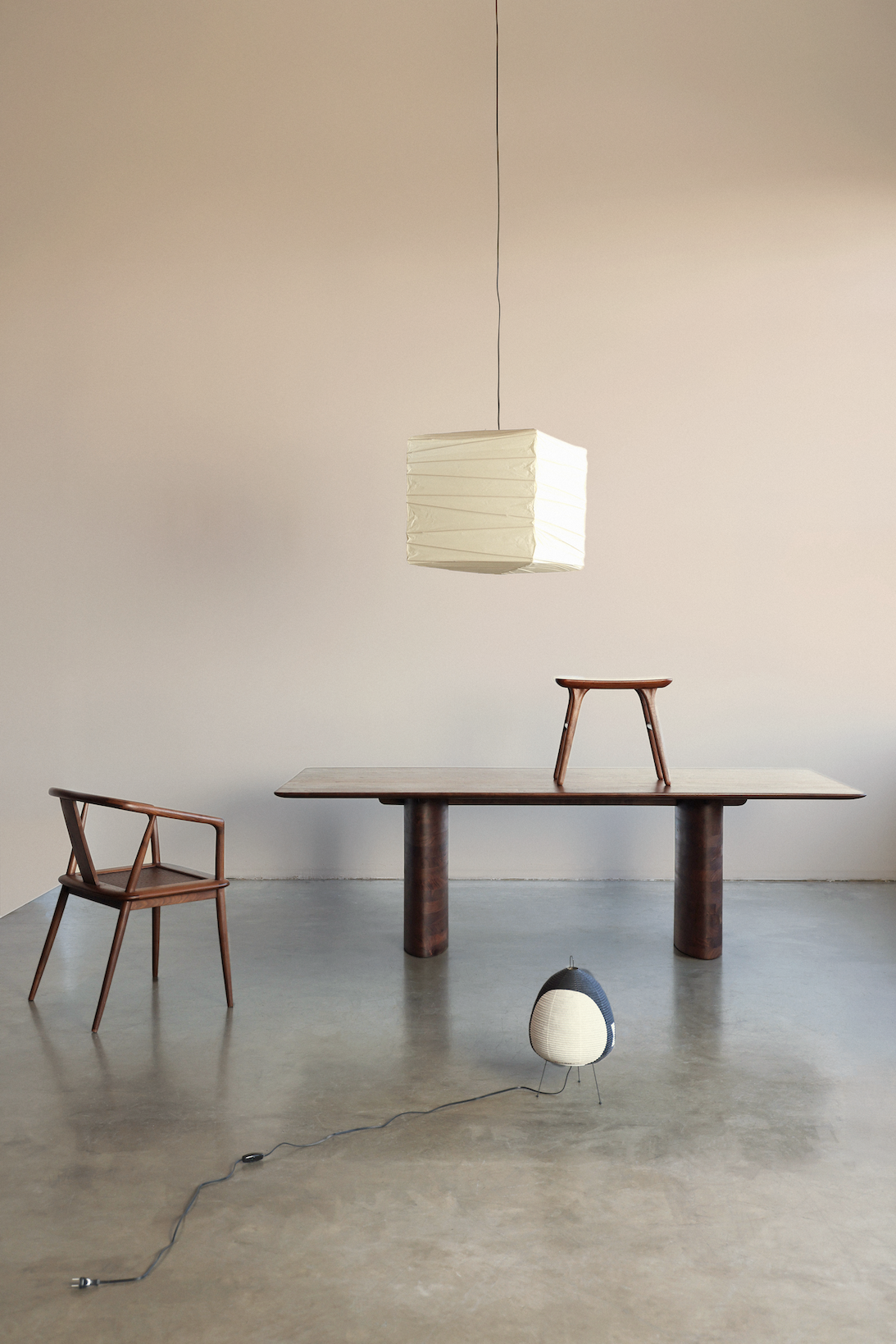 Minimalist room with wooden chair, table with stool on top, hanging square lamp, and floor lamp with cord.