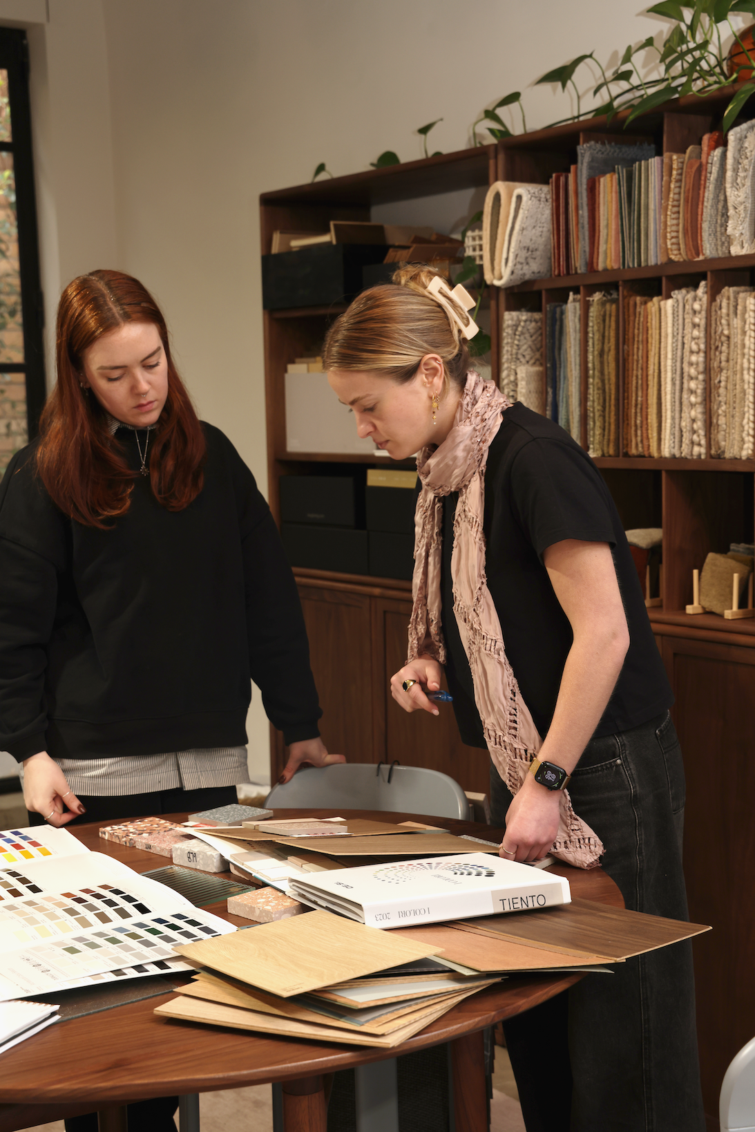 Two women reviewing flooring and paint samples on a table in a design studio.