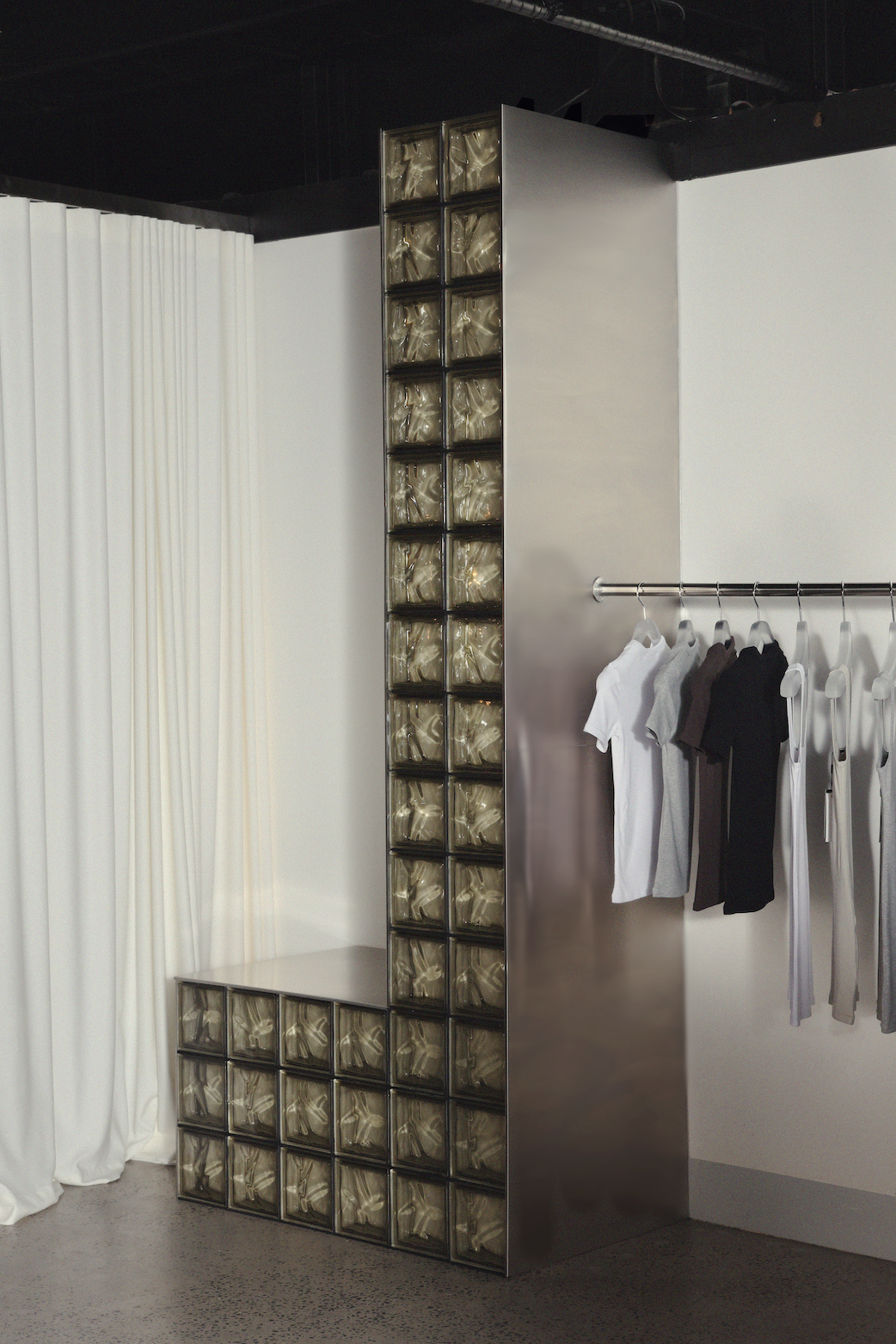 Modern bench with built-in glass blocks and nearby clothing rack with hanging shirts in a minimalist room.