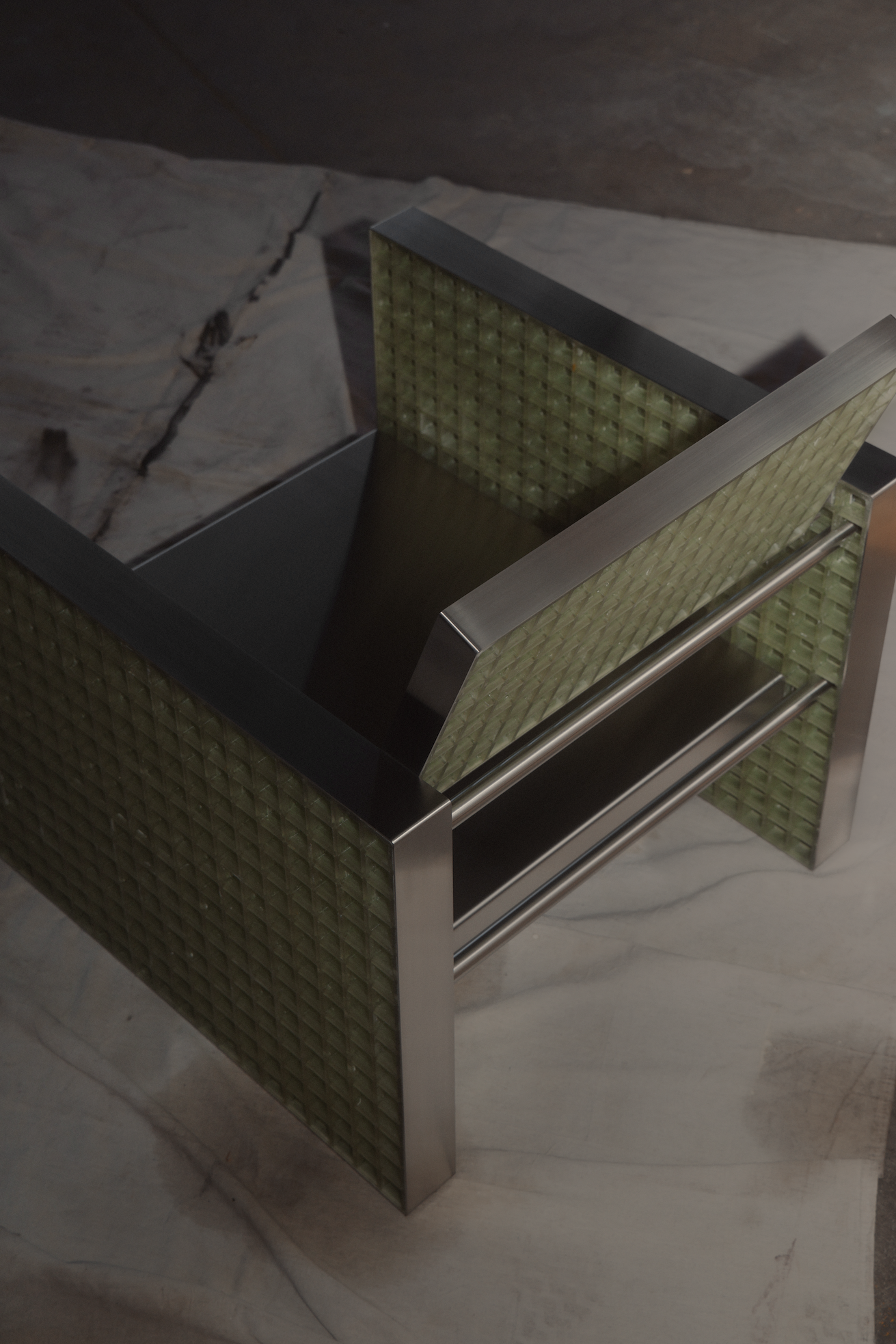 Modern chair with green textured panels and brushed metal frame on a concrete floor.