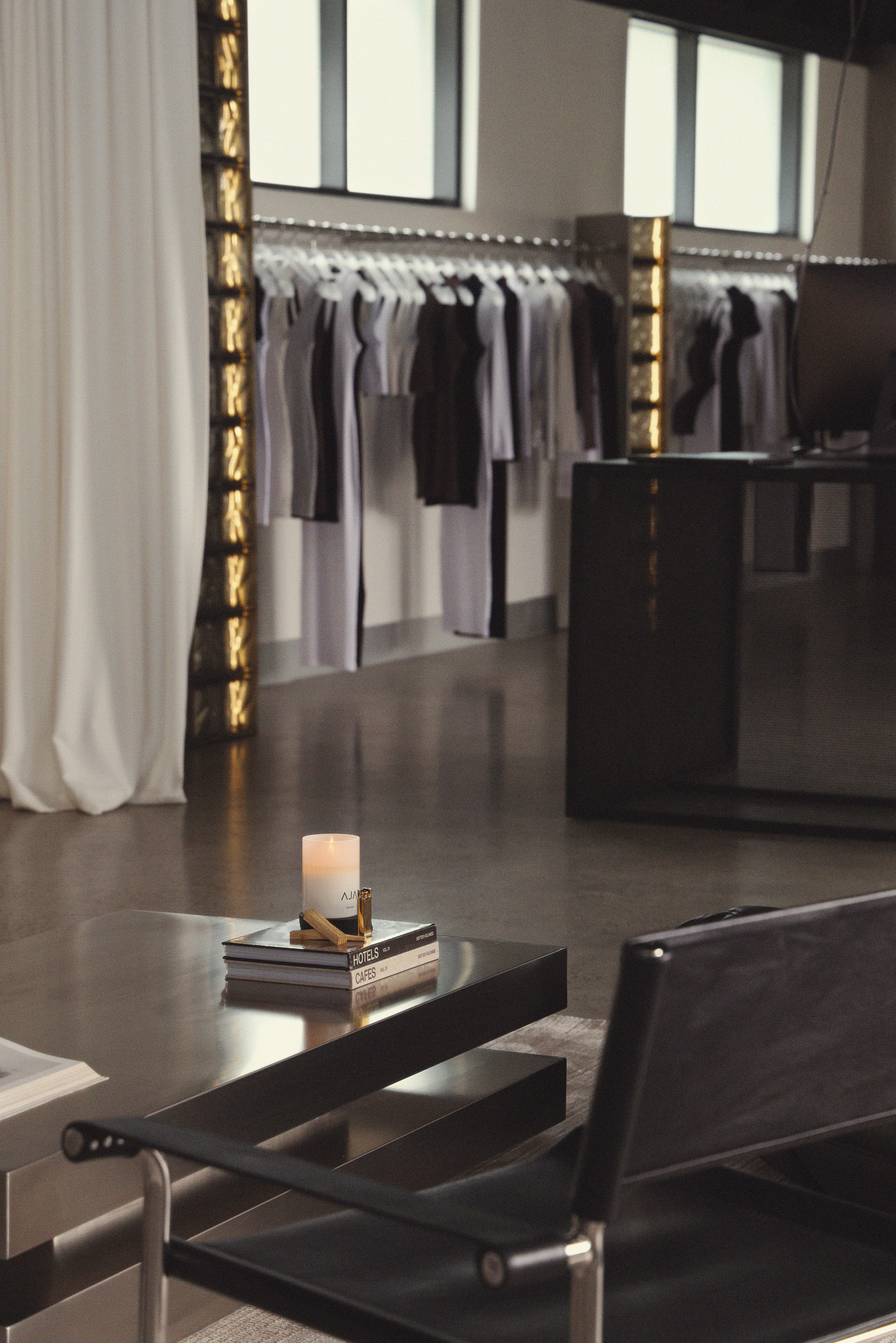Modern boutique interior with black and white dresses on racks, a lit candle, and black chair by metal table.