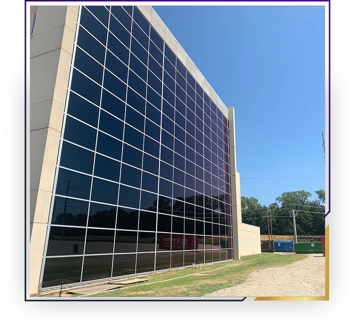 Modern building facade with large dark reflective glass panels reflecting trees and a power line under a clear blue sky.