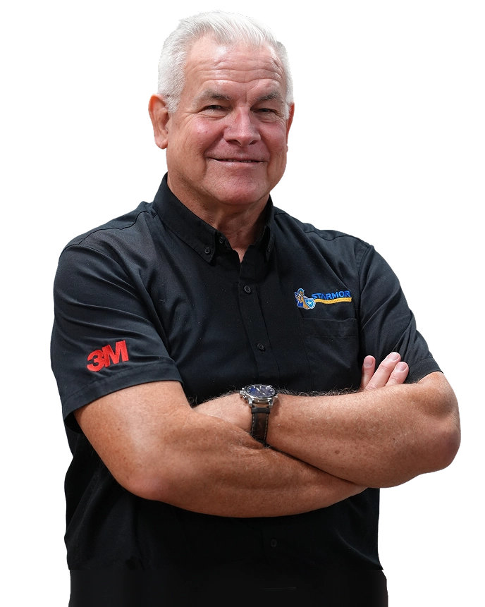 Smiling older man with white hair, wearing a black shirt with 3M and Starmor logos, arms crossed.