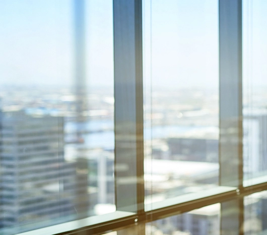 Cityscape view through a large office window with sunlight reflection.