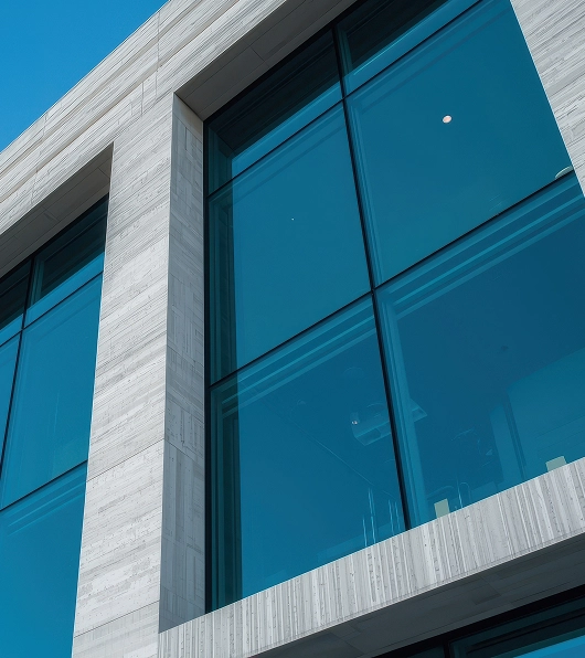 Modern building facade with large reflective glass windows and beige stone framing against a clear blue sky.