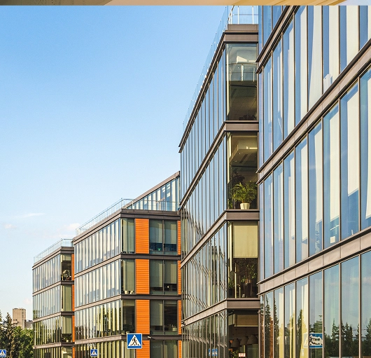 Modern office buildings with large glass windows reflecting the blue sky.