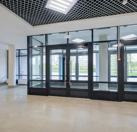 Modern building entrance with glass double doors and large windows allowing natural light inside.