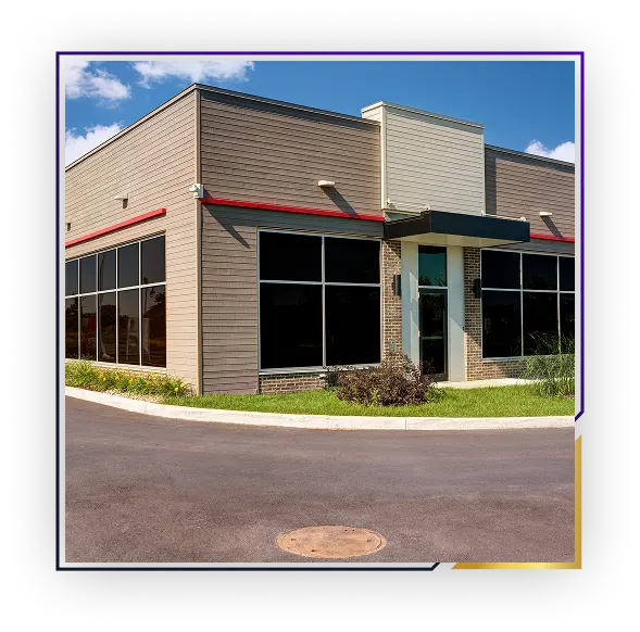 Modern commercial building with large dark windows, beige siding, and a black entrance canopy on a sunny day.