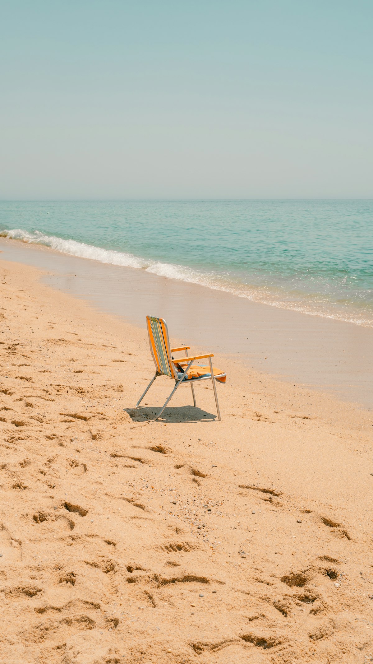 A single empty beach chair sitting alone on a quiet shoreline, evoking a team member fully unplugged on vacation while Atlassian automation quietly holds down the fort back at work. Photo by Aleksandr Zaitsev on Unsplash.
