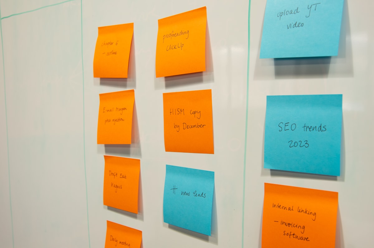 Close-up of a whiteboard covered in orange and blue sticky notes arranged like a kanban board, illustrating Trello boards now reachable by AI assistants. Photo from Unsplash.