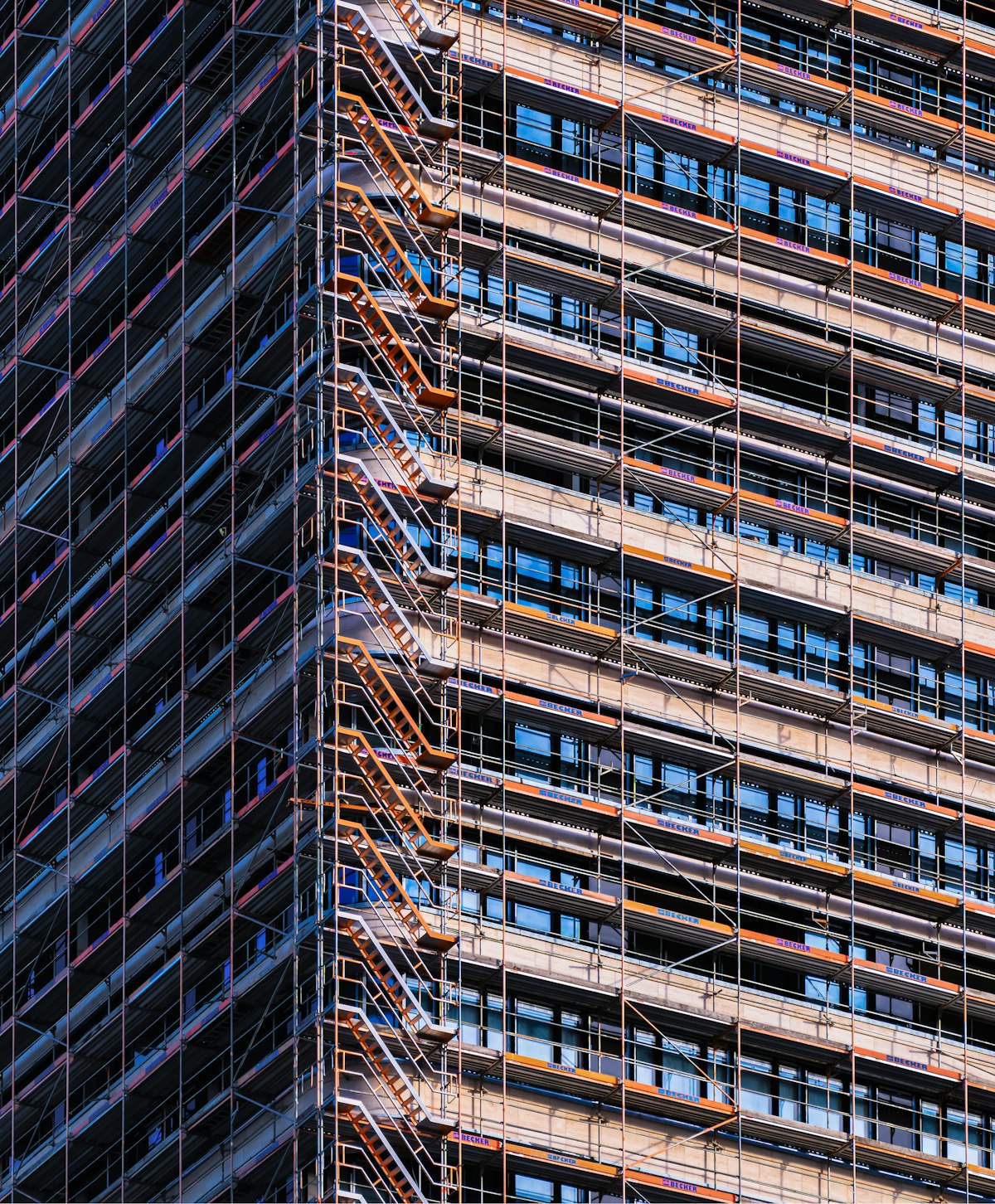 Orange scaffolding wrapped around a modern glass building under construction, the support structure surrounding the finished work