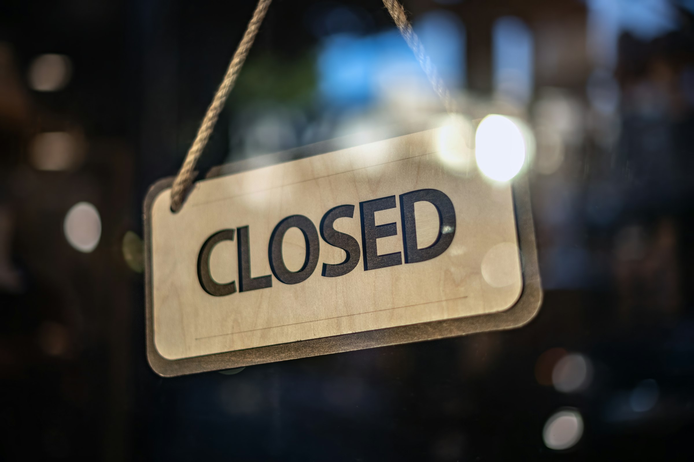 A CLOSED sign hanging in the glass door of a darkened storefront at night, with lights still visible inside