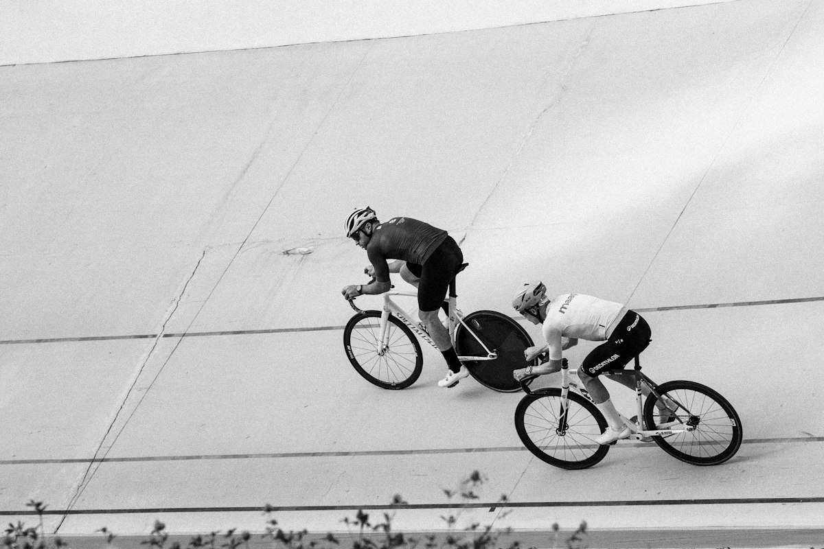 Cyclists racing on a banked velodrome track, the curved walls holding a continuous loop on course
