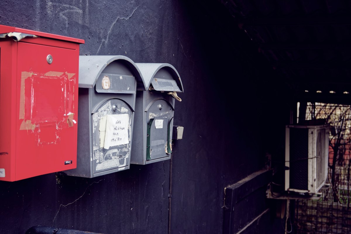 A row of red and grey mailboxes mounted along the side of a building, a nod to Atlassian Cloud release notes moving to a new address. Photo from Unsplash.