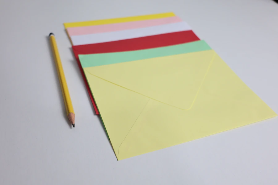 Coloured envelopes and a pencil arranged on a white surface