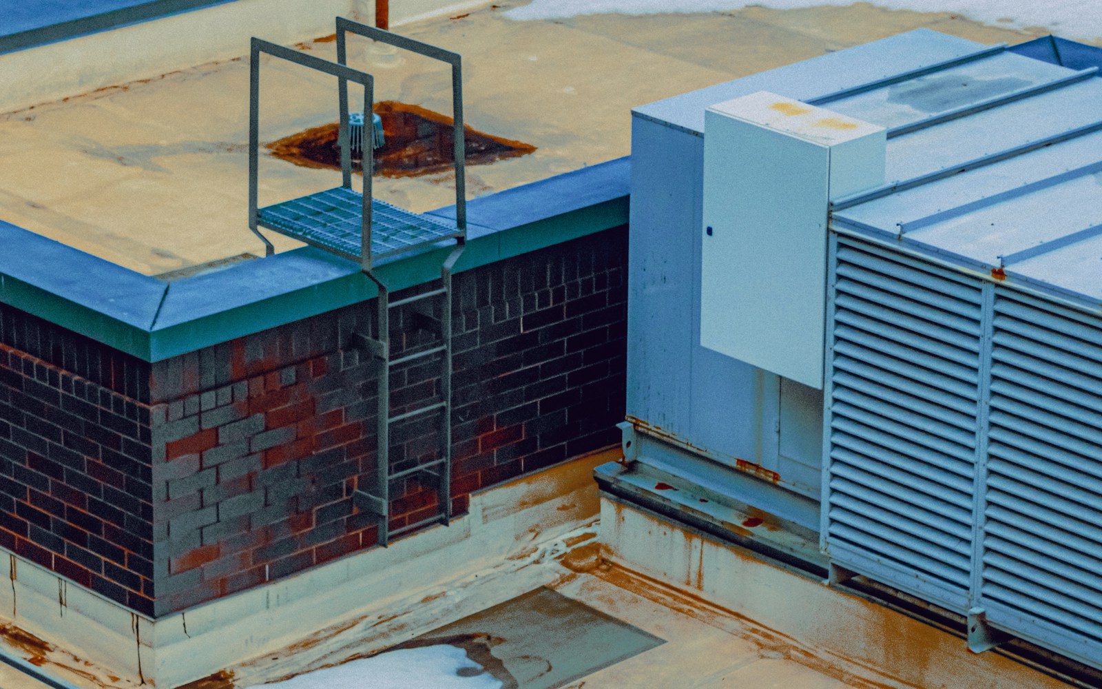 HVAC equipment and an access ladder on a commercial rooftop with patches of snow. Photo by Linus Belanger on Unsplash.