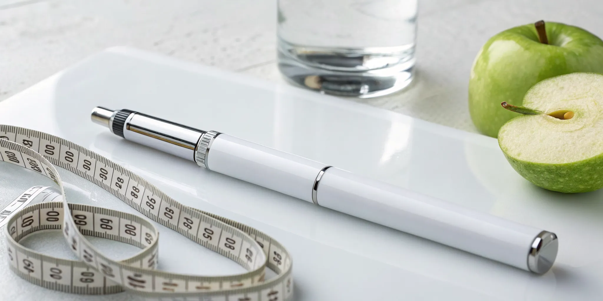 GLP-1 weight loss therapy pen with a measuring tape, green apple, and water.