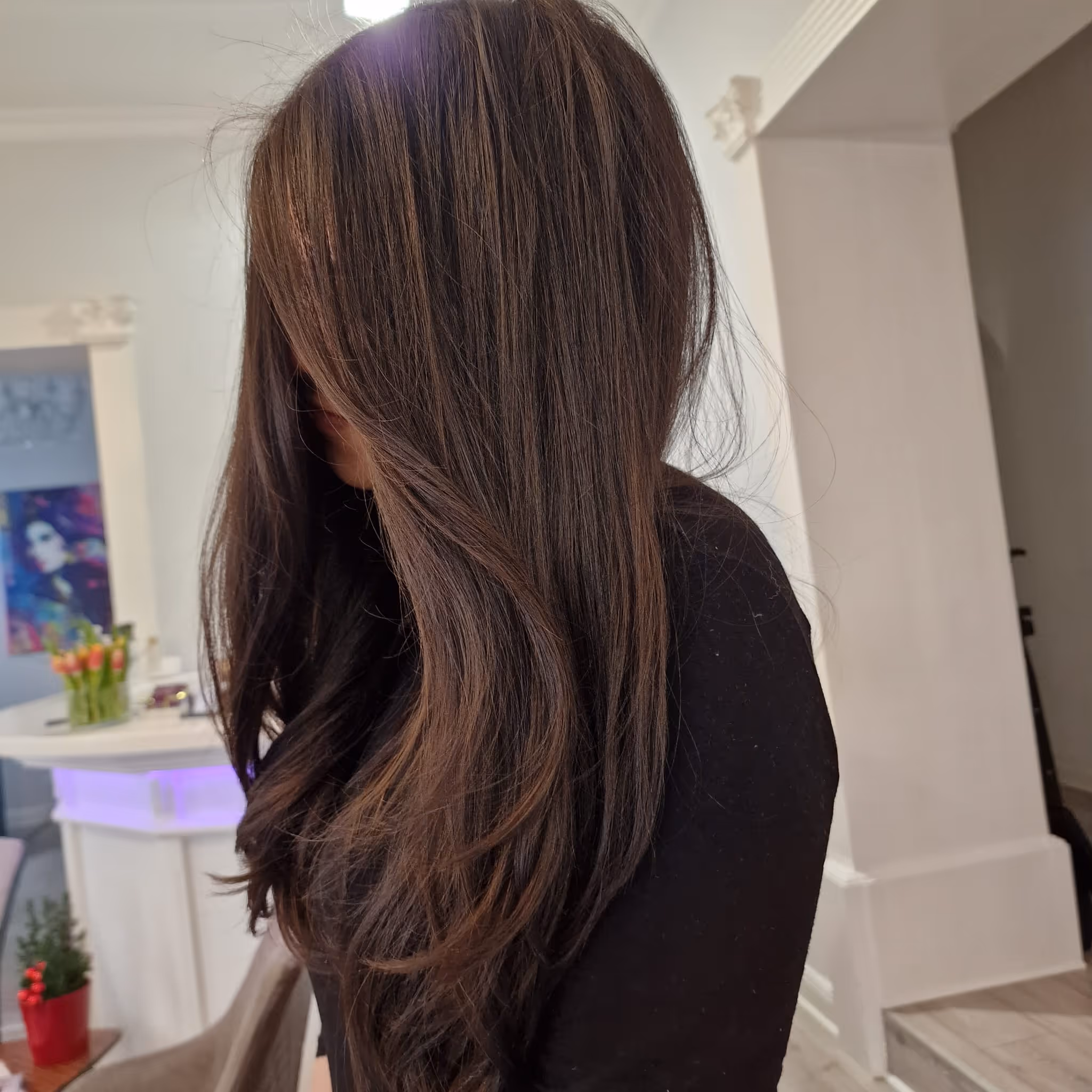 Kundin im Friseursalon mit Foliensträhnen im Haar, während die Stylistin ein Spiegel-Selfie macht.