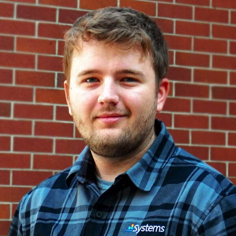 Systems IT consultant smiling in front of brick wall wearing branded plaid shirt for Billings MT managed service provider