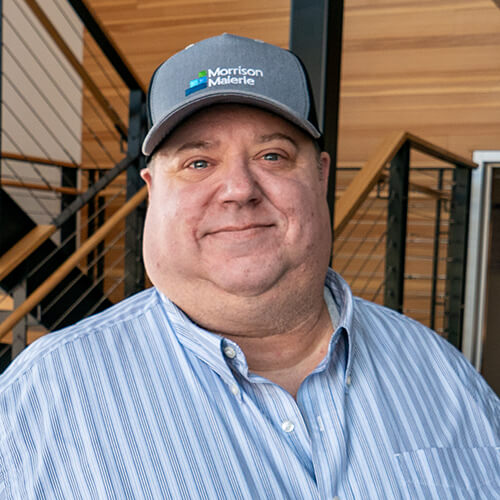Morrison Malertic IT professional smiling in branded cap inside modern office building
