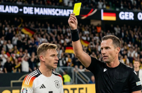 Bir futbol maçı sırasında hakem, Almanya milli takımından bir oyuncuya sarı kart gösteriyor.