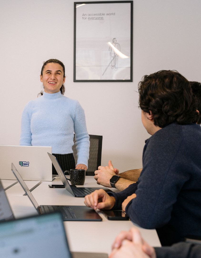 Woman presenting in a meeting about accessibility while colleagues listen around a table.