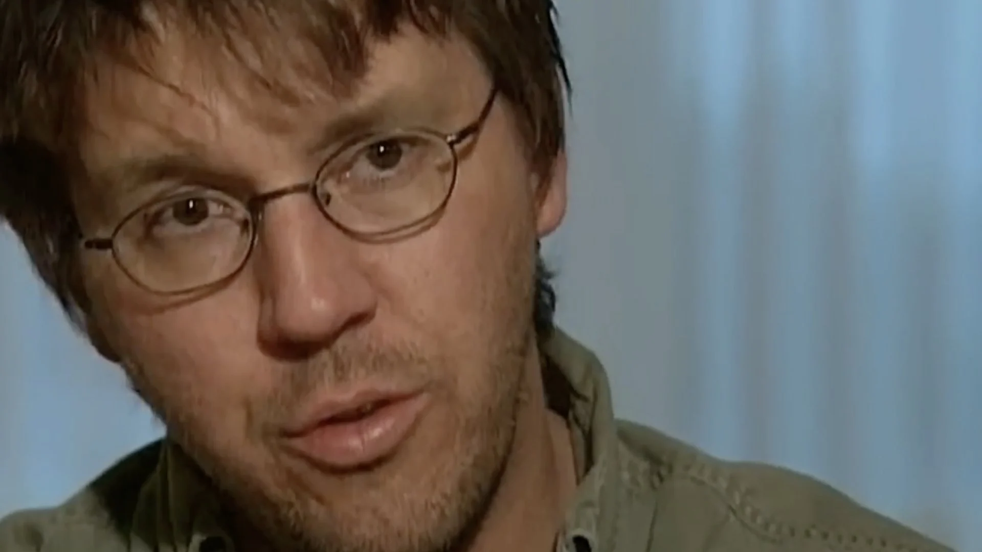 Close-up of a man with glasses wearing a green shirt against a soft blue background.