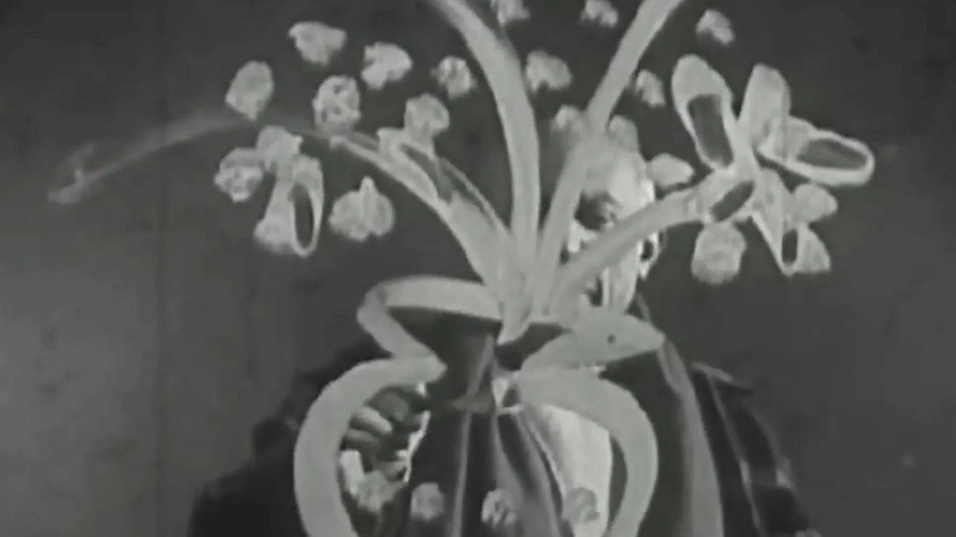 Black and white image of a person holding a bouquet with stylized large flowers and leaves partially obscuring their face.