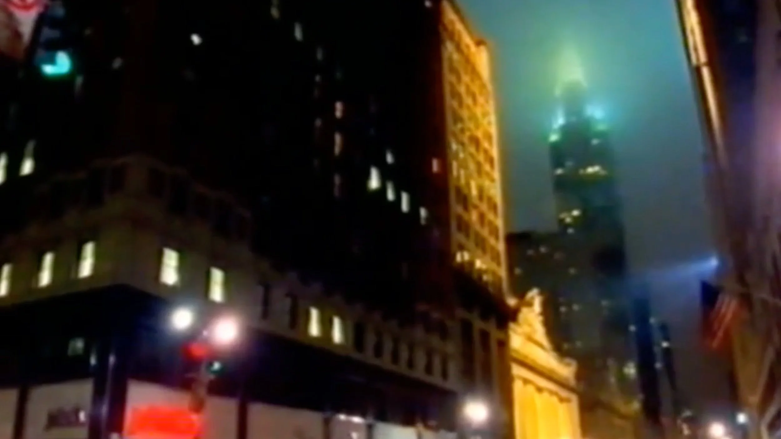 Nighttime cityscape showing illuminated buildings and a skyscraper with blue lights shining through fog.