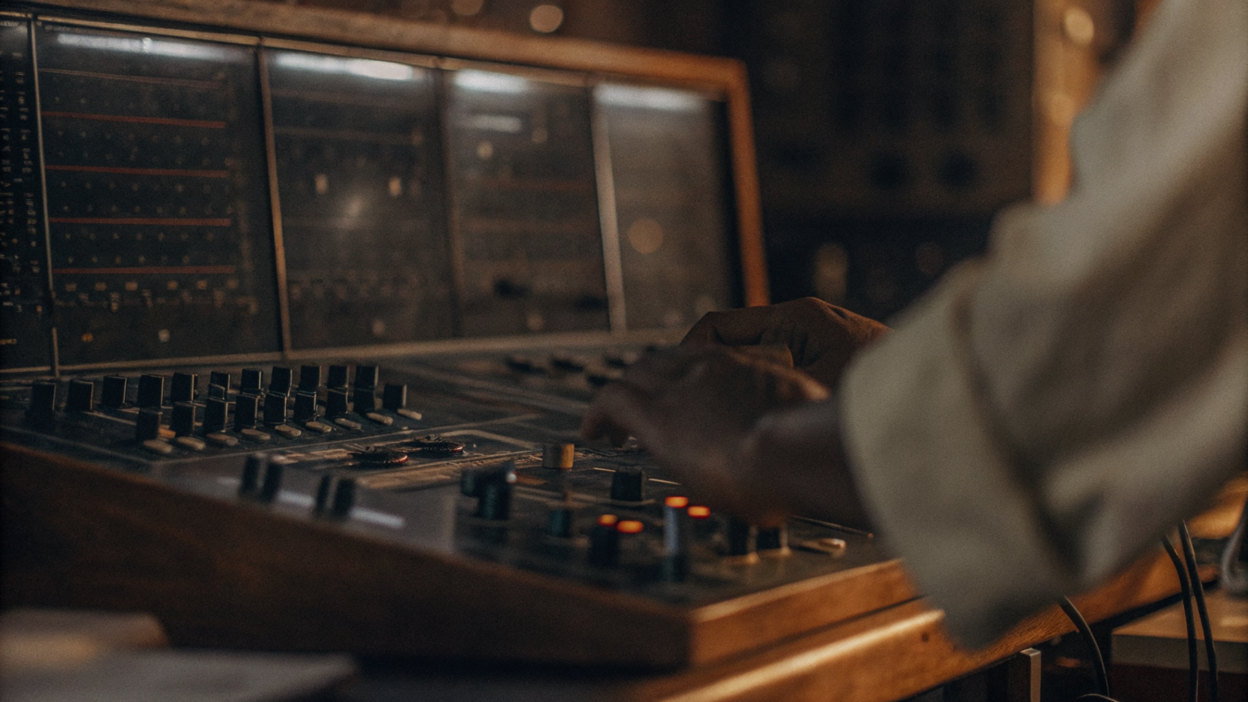 Person bedient ein analoges Mischpult in einem Tonstudio – warme, dunkle Atmosphäre mit Reglern und Monitoren im Hintergrund.