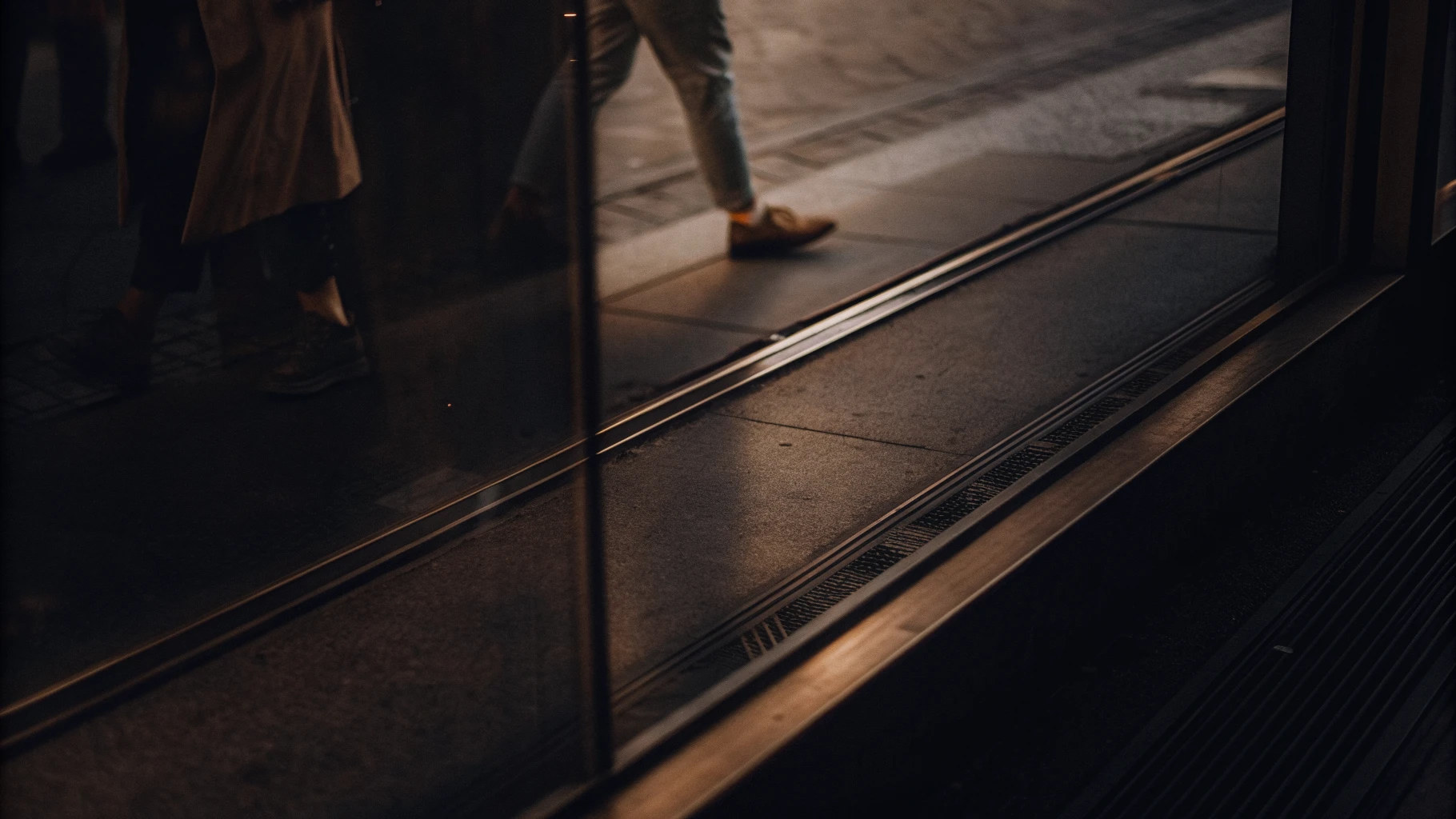 Blick durch eine Glasscheibe auf einen Gehweg, die Spiegelung zeigt Passanten versetzt zur tatsächlichen Szene
