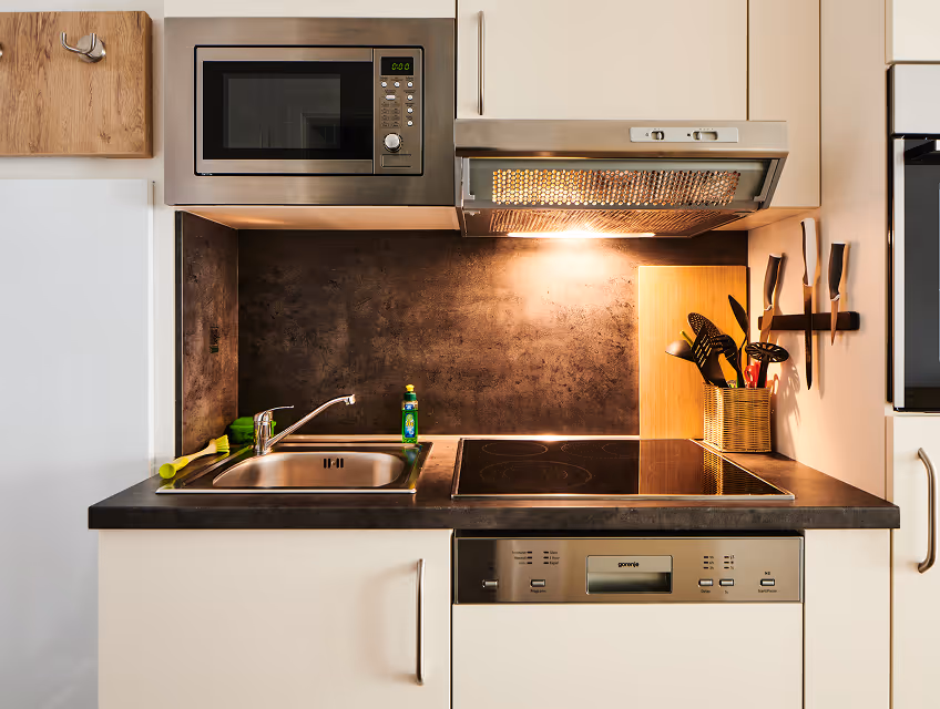 Modern kitchen countertop with a sink, microwave, stovetop, under-cabinet light, and cooking utensils in a holder.