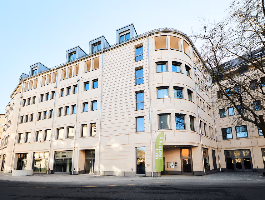 Modern beige apartment building with multiple windows and a green banner reading 'ADAPT APARTMENTS' near the entrance.