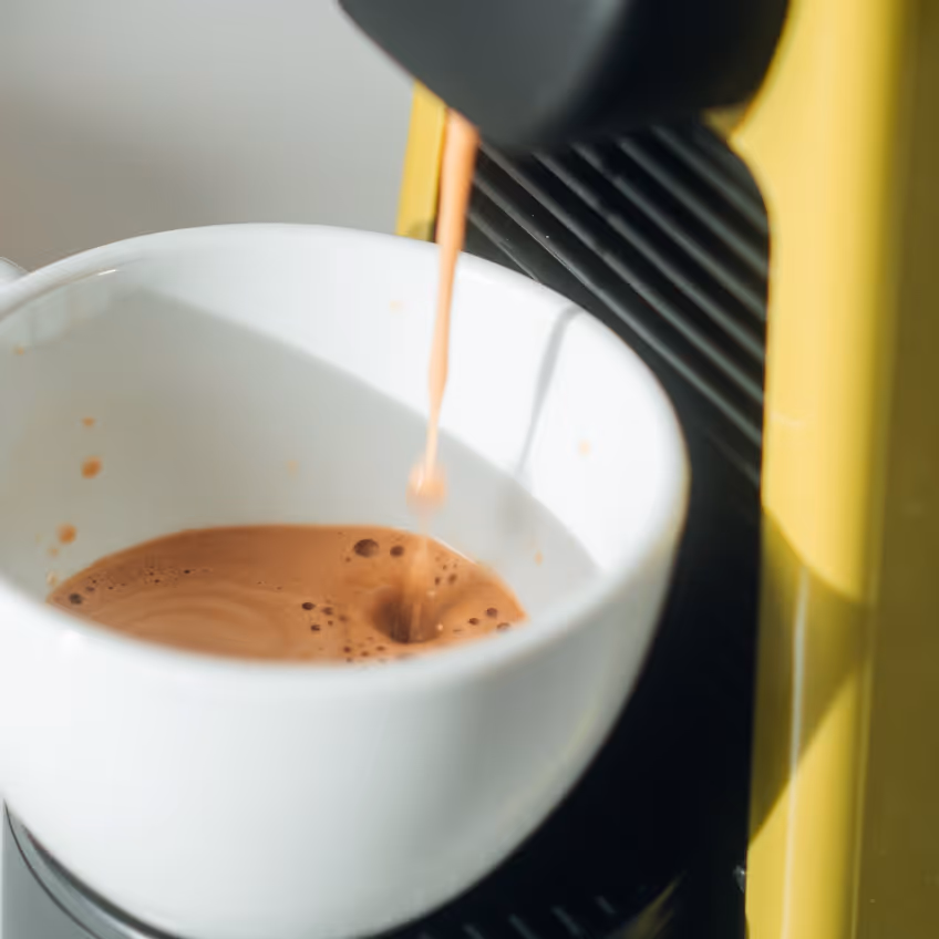 Close-up of a coffee machine dispensing espresso into a white cup.