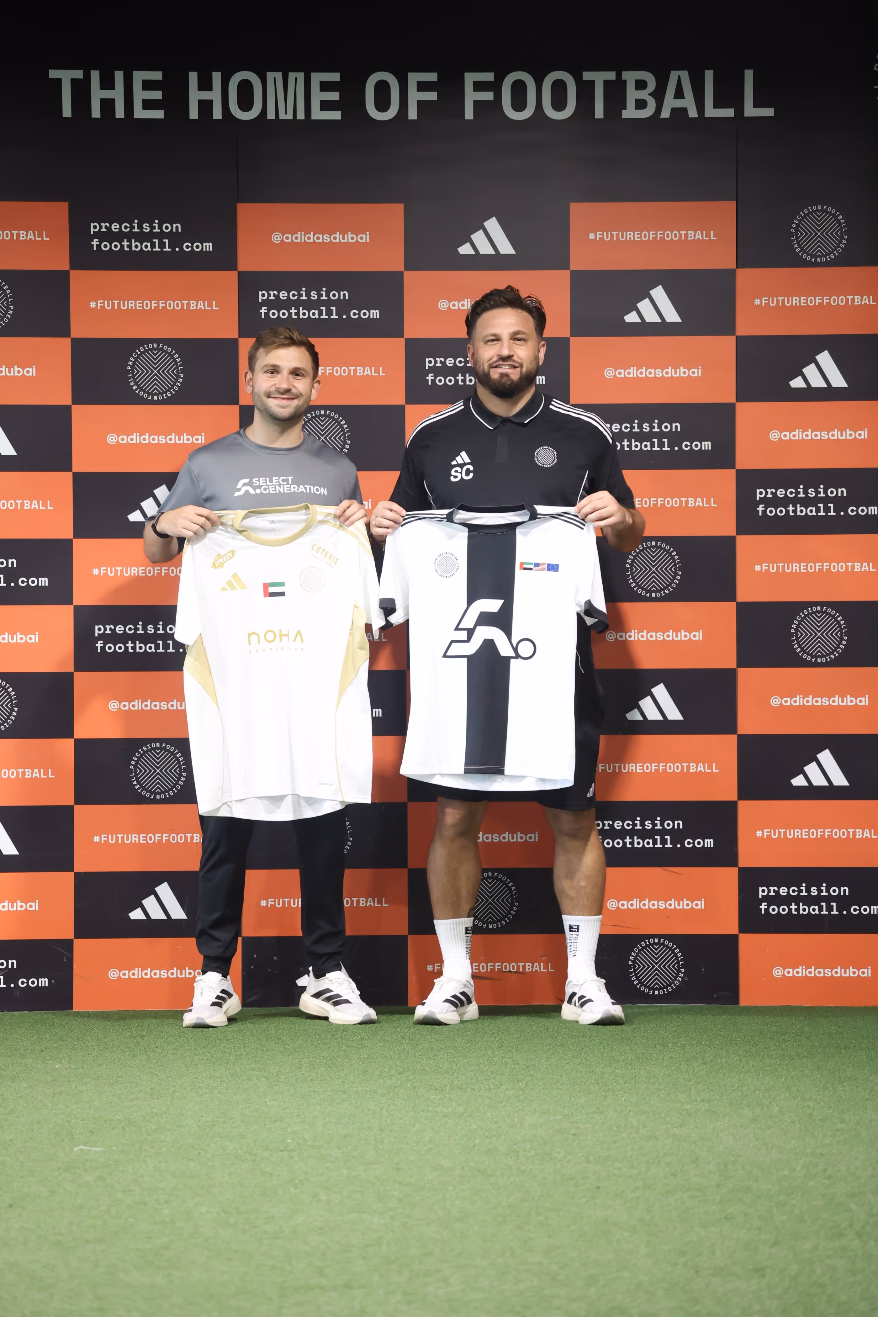 Two soccer players in white and maroon uniforms running towards a soccer ball on a grassy field during a match, with a referee in the background.