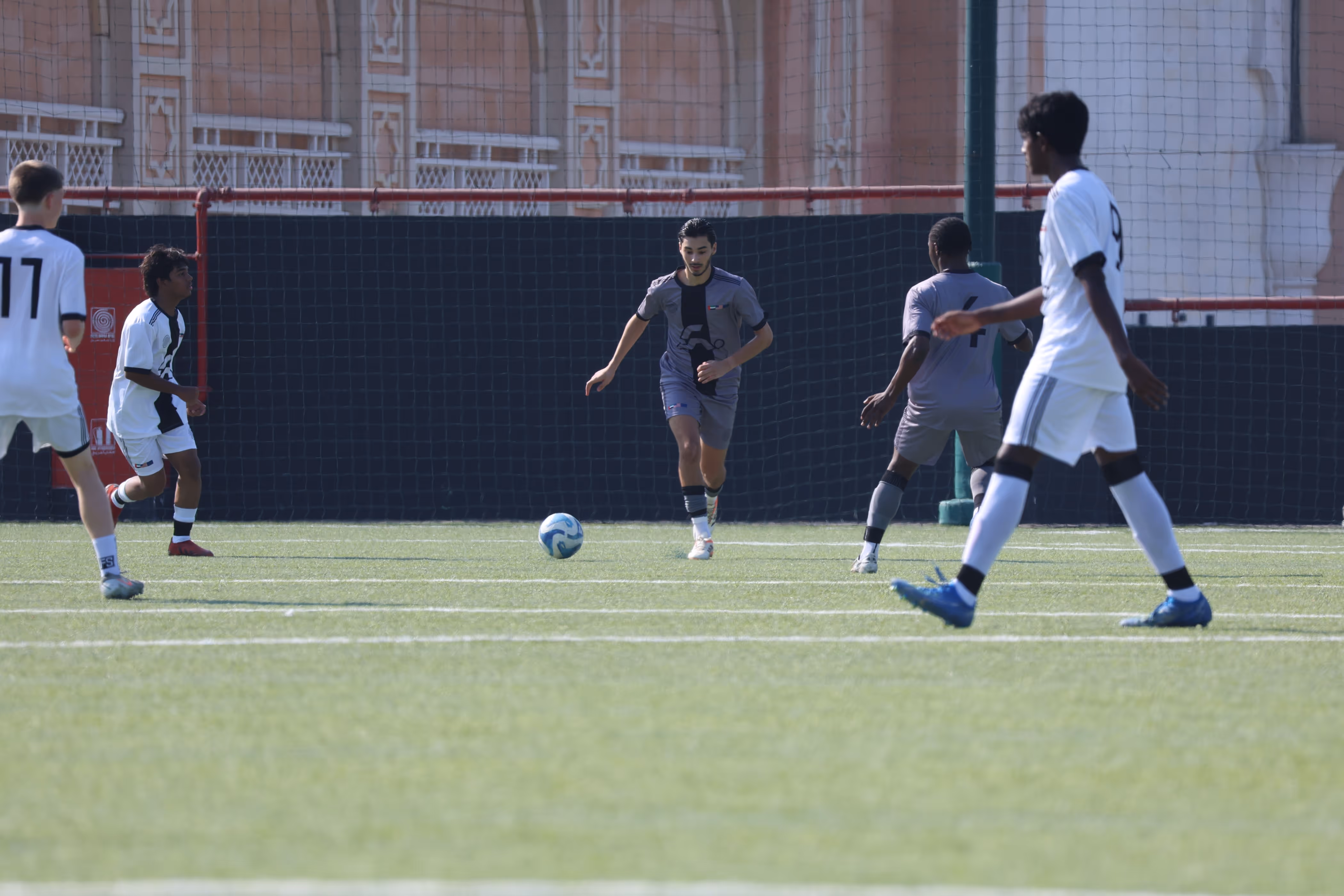 Soccer players from two teams jumping to head the ball on a green field, with players in maroon and white uniforms.