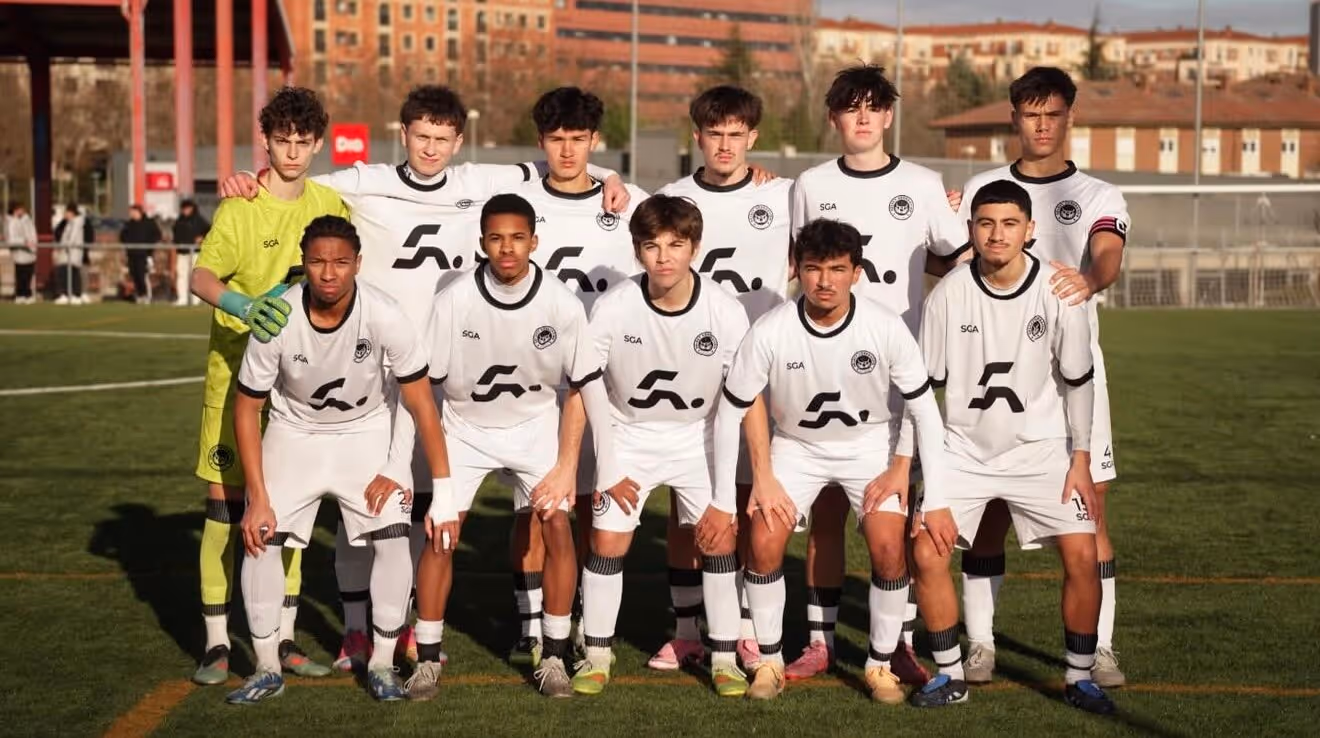 Soccer players from two teams jumping to head the ball on a green field, with players in maroon and white uniforms.