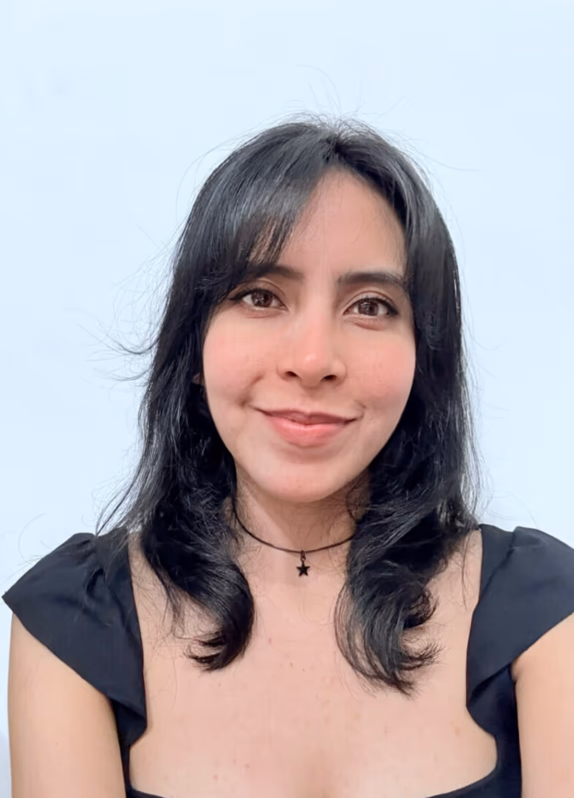 Smiling woman with shoulder-length black hair wearing a black top and star pendant necklace against a plain light background.