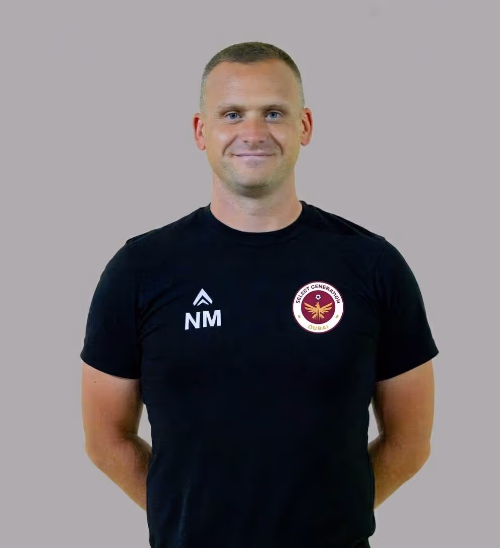 Man wearing a black polo shirt standing outdoors on a grassy field.