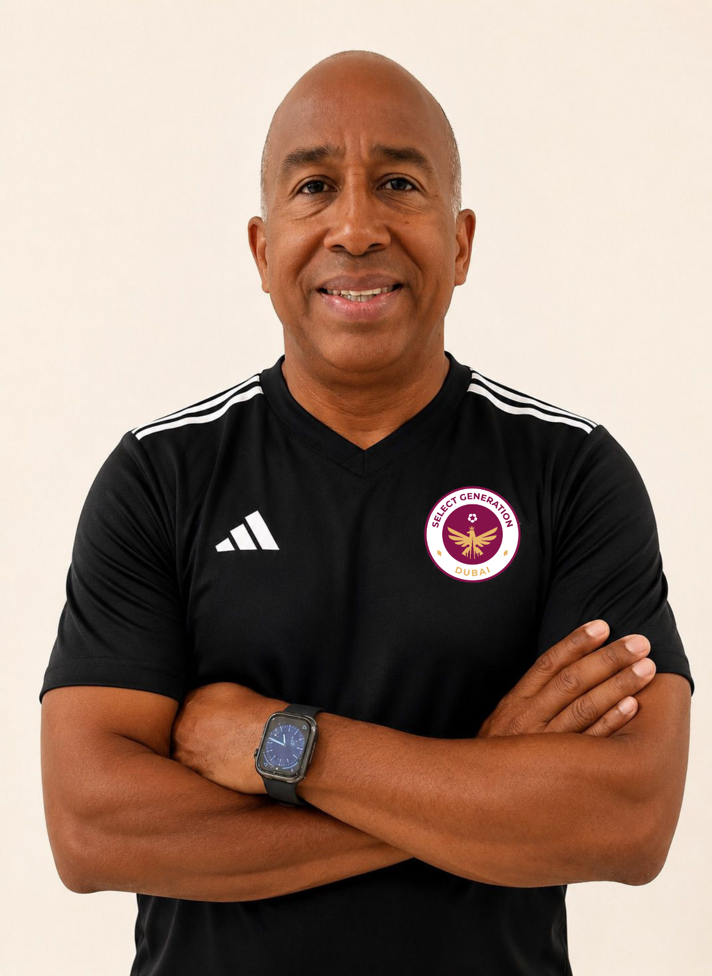 Man with arms crossed wearing a black Adidas t-shirt and a black cap against a plain light background.
